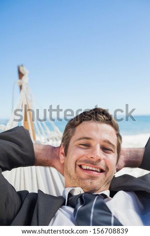Smiling businessman relaxing in hammock looking at camera on sunny day