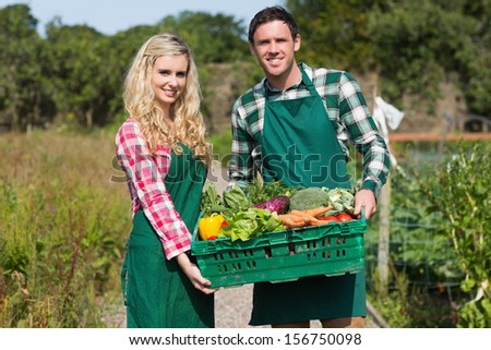 Happy couple showing vegetables in their garden while looking at the camera