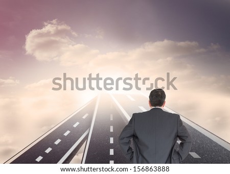 Composite image of businessman standing back to the camera with hands on hip on streets floating in sky