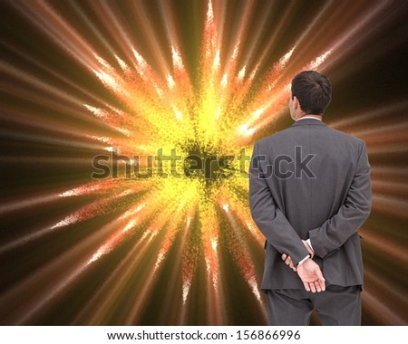 Composite image of businessman standing with hands behind back looking at yellow orange firework background