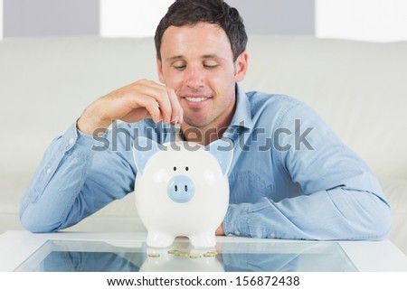Content casual man putting coin in piggy bank in bright living room