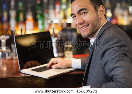 Smiling businessman working on his laptop while having a drink in a classy bar