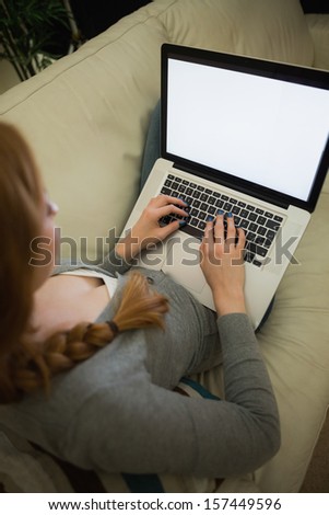 Redhead sitting on the sofa using her laptop at night at home in the sitting room