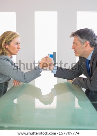 Two annoyed mature businesspeople having an arm wrestling sitting around a table at office