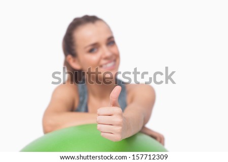 Pony tailed woman showing thumbs up supporting herself with a fitness ball