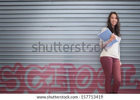 Happy student holding notebook posing on graffiti background