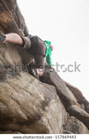 Determined man climbing a large rock face and seeing the summit and the bright sky