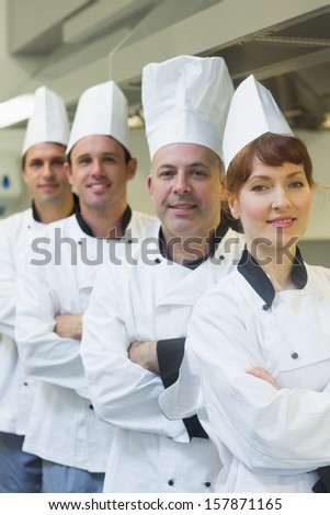 Four happy chefs smiling at the camera wearing uniforms posing in a kitchen