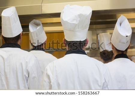 Five chefs standing in a kitchen turning their back on the camera