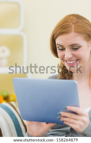 Cheerful redhead sitting on the couch using tablet at home in the sitting room