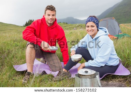 Couple cooking outside on camping trip smiling at camera in the countryside