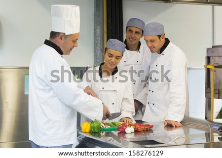 Smiling head chef teaching how to slice vegetables to his students in kitchen