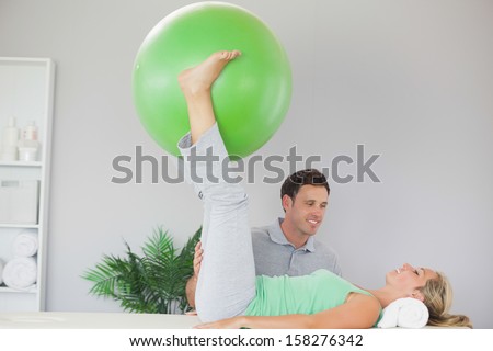 Patient holding exercise ball between legs in bright office