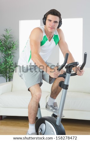 Content handsome man training on exercise bike listening to music in bright living room