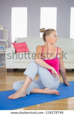 Sporty focused blonde sitting on blue exercise mat in bright living room