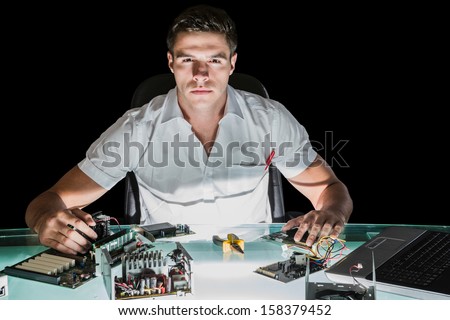Handsome stern computer engineer working by night at his lit desk