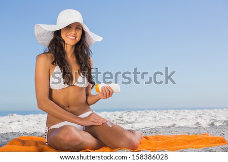 Attractive woman on the beach applying sun cream while sitting on her towel