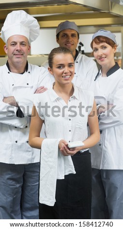 Waitress standing in front of team of chefs smiling at camera