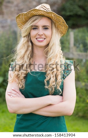 Pretty woman wearing a straw hat folding her arms in her garden