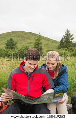 Cheerful couple taking a break on a hike to look at map in the countryside