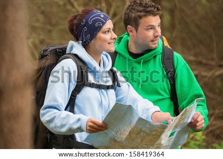 Smiling couple standing in a forest holding map on a hiking trip
