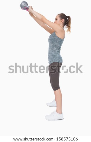 Profile view of pony tailed woman training with a kettle bell on white screen