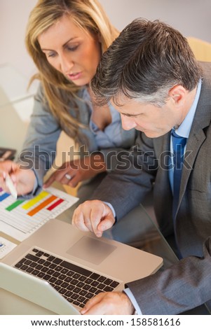 A blonde businesswoman and a mature businessman looking at laptop in an office