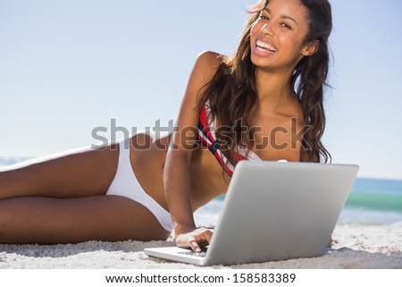 Happy attractive young woman in bikini with her laptop on the beach
