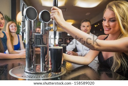 Attractive woman pulling a pint of stout in front of her friends in a restaurant