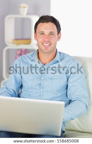 Happy casual man sitting on couch using laptop in bright living room