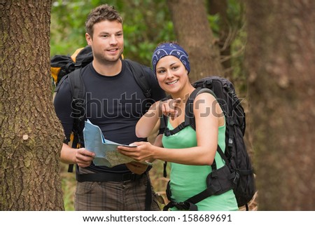 Fit couple reading map in a forest with woman pointing in a forest