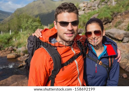 Couple wearing rain jackets and sunglasses smiling at camera in the countryside