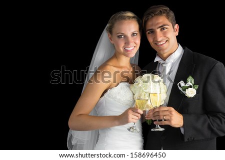Happy young married couple posing holding champagne glasses on black background