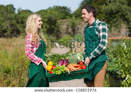 Young couple carrying vegetables in their garden smiling at each other