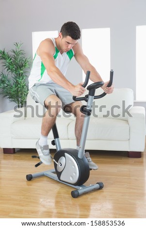 Sporty handsome man training on exercise bike in bright living room