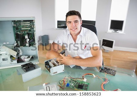 Nice looking computer engineer sitting at desk smiling at camera in bright office