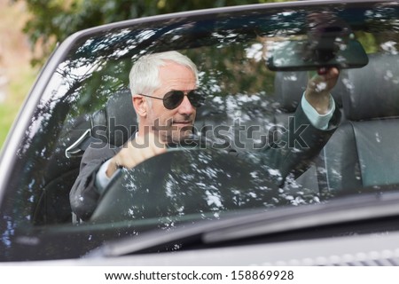 Mature businessman adjusting his cabriolet rear view mirror while driving