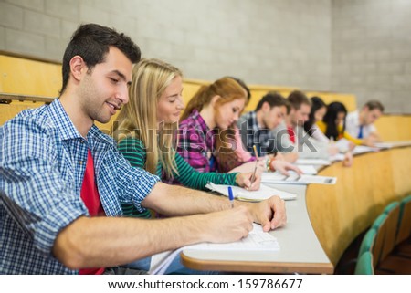 Side view of students writing notes in a row at the college lecture hall