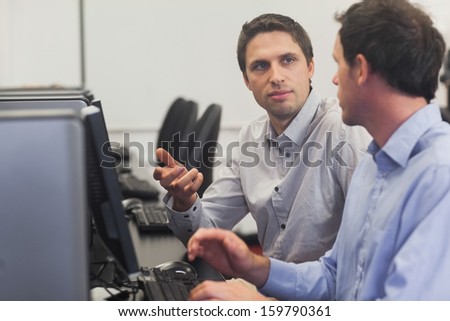 Two handsome men talking while sitting in computer class pointing at monitor