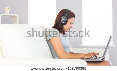 Cute casual woman witting on couch using her notebook and listening to music in the living room