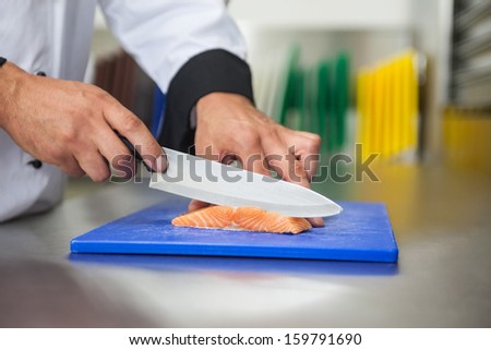 Chef slicing raw salmon with knife on blue cutting board in professional kitchen