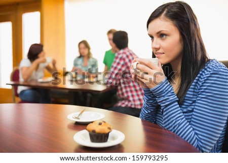 Female having coffee and muffin with students around table in background at  the coffee shop