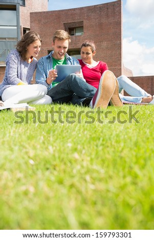 Group of young students using tablet PC in the lawn against college building