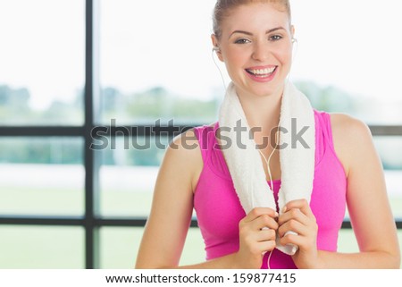Portrait of a smiling young woman with towel around neck listening to music in fitness studio
