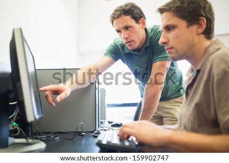 Side view of teacher showing something on screen to mature student in the computer room