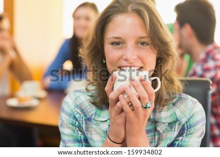Close-up of a smiling female having coffee with students in background at  the coffee shop