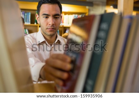 Close-up of a serious mature student selecting book from shelf in the library