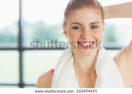 Close up of a smiling woman with towel around neck listening to music in fitness studio