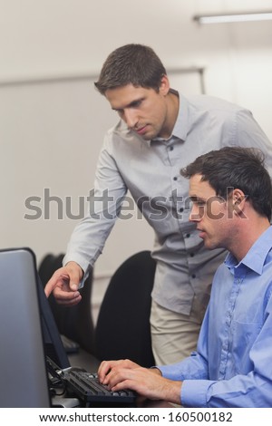 Handsome teacher talking to a student in computer class