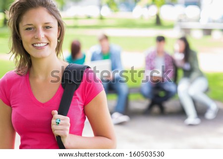 Portrait of college girl smiling with blurred students sitting in the park